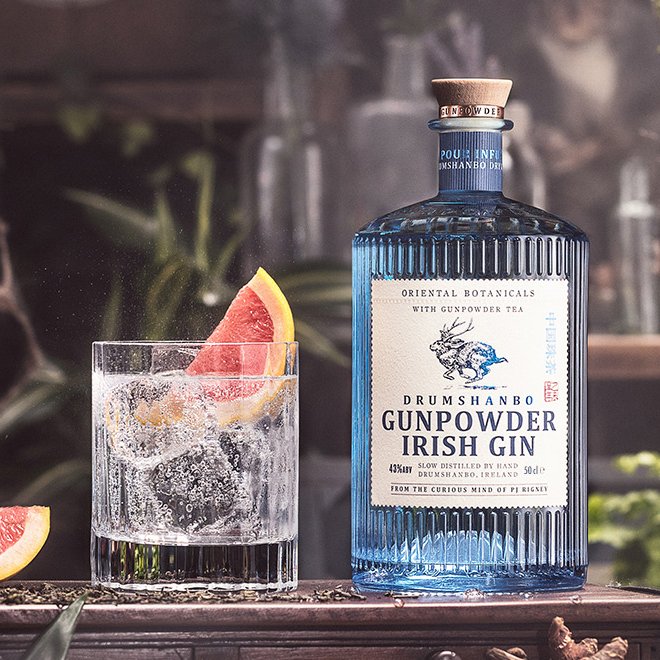 Das Bild zeigt Den Gunpowder Irish Gin neben Cocktail vor dunklem Hintergrund.