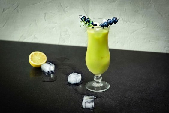 Das Bild zeigt einen grünen Cocktail mit Heidelbeerdeko